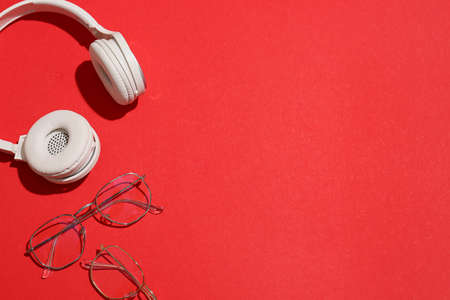 Stylish eyeglasses and modern headphones on red backgroundの写真素材