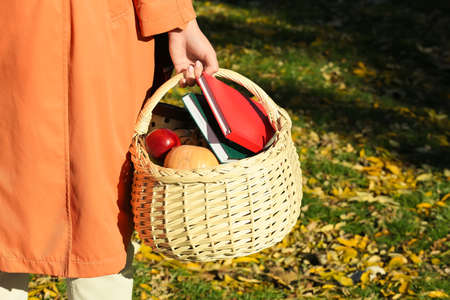 Woman holding picnic basket with fruits, vegetables and books outdoorsの写真素材