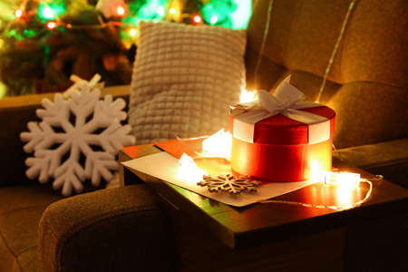 Armrest table with Christmas gift, snowflake and glowing lights on armchair in roomの写真素材