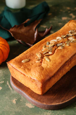 Wooden board with tasty pumpkin pie on green background