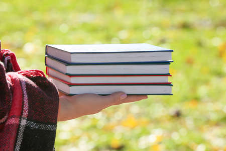 Woman with plaid holding stack of different books on sunny autumn dayの写真素材