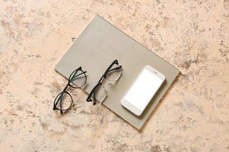 Eyeglasses, mobile phone and notebook on color background