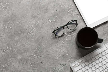 Eyeglasses, cup of coffee, tablet computer with keyboard on gray background