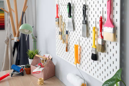 Pegboard with putty knives and brushes on light wall in decorator's workshop