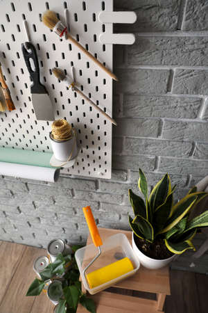 Stepladder stool with paint roller, houseplant and pegboard with decorator's tools on gray brick...