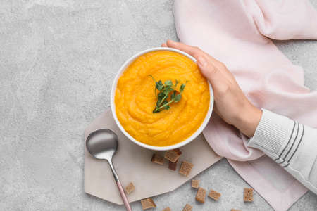 Woman holding bowl of tasty pumpkin cream soup on gray backgroundの写真素材
