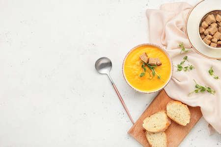 Bowl of tasty pumpkin cream soup and bread on white background
