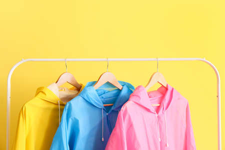 Rack with colorful raincoats near yellow wall