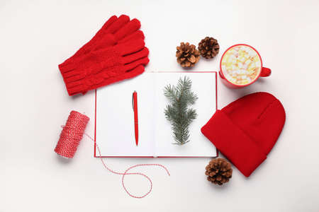 Beautiful winter composition with open notebook, gloves, hat and cup of cacao on white background