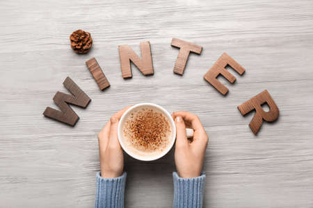 Female hands with cup of cacao and word WINTER on gray wooden backgroundの写真素材