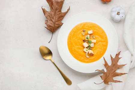 Composition with plate of tasty pumpkin cream soup and autumn leaves on white backgroundの写真素材