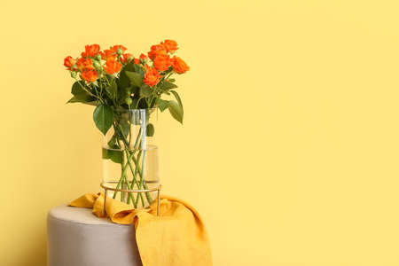 Vase with beautiful orange roses on pouf against yellow wallの写真素材