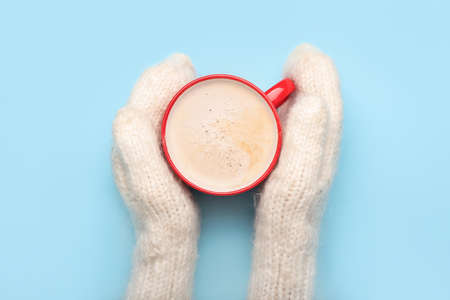 Female hands in knitted mittens and cup of tasty cacao on color background, closeupの写真素材