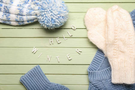 Text HELLO WINTER and warm clothes on color wooden background, closeupの写真素材