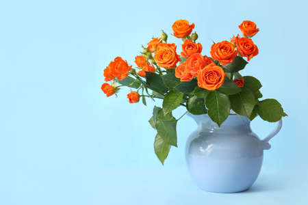 Jug with beautiful orange roses on blue backgroundの写真素材
