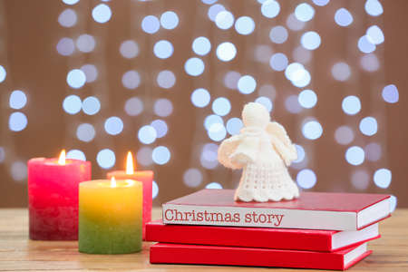 Books with angel toy and glowing candles on table against blurred lights. christmas storyの写真素材