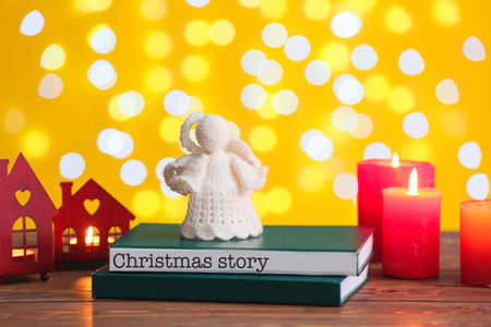 Books with angel toy and glowing candles on table against blurred lights. christmas storyの写真素材