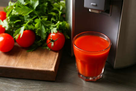 New modern juicer and glass of fresh juice with tomatoes on table, closeupの写真素材