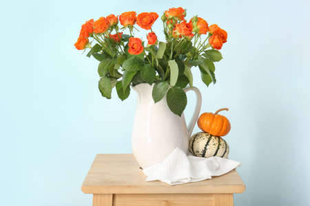 Jug with beautiful orange roses and pumpkins on table against blue wallの写真素材