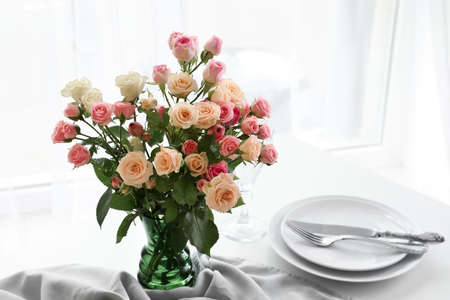Vase with beautiful roses on served table in light room
