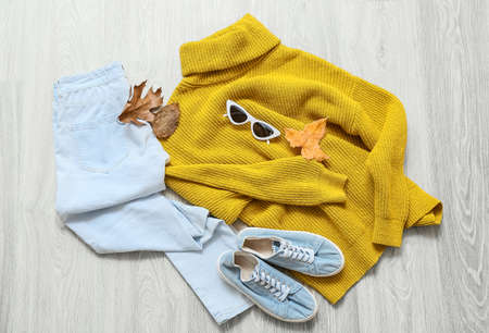 Stylish female sweater, jeans, shoes, sunglasses and autumn leaves on light wooden background