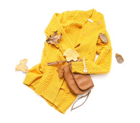 Stylish knitted cardigan, accessories and autumn leaves on white background