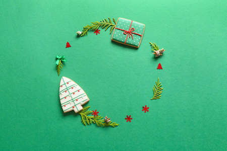Frame made of fir branches and Christmas cookies on green background