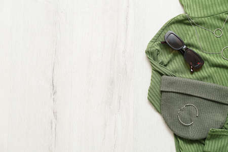 Stylish sweater, hat, sunglasses, bracelet and necklace on light wooden background