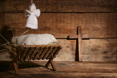 Manger with baby, angel and cross on wooden background. Concept of Christmas story