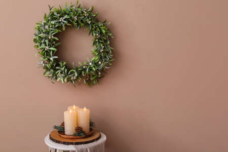 Burning candles on table and beautiful wreath with mistletoe hanging on brown wallの写真素材