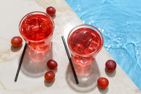 Glasses of fresh grape soda on edge of swimming pool