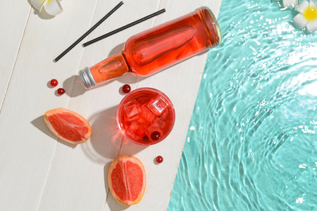 Bottle and glass of fresh soda near swimming pool