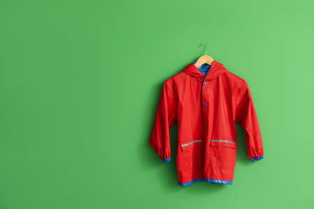 Red children's raincoat hanging on green wallの写真素材