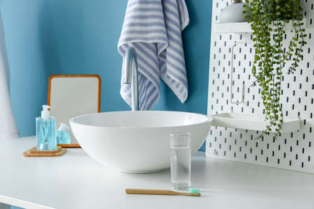 Table with sink, glass of water, toothbrush and pegboard near blue wall