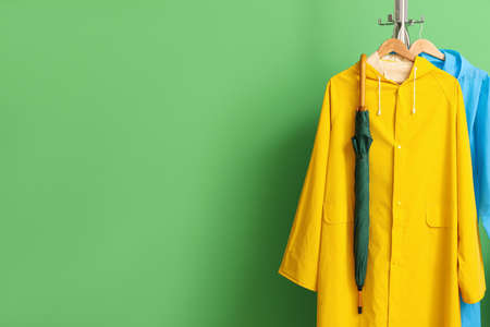 Rack with raincoats and umbrella near green wallの写真素材
