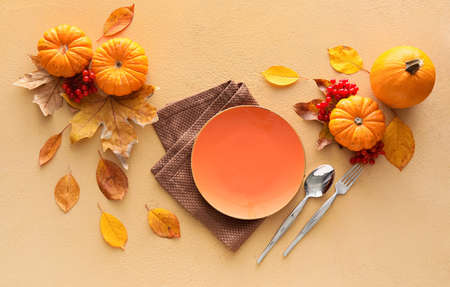 Composition with table setting, pumpkins and autumn leaves on beige backgroundの写真素材