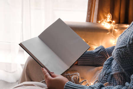 Woman sitting on sofa with glowing lights and holding opened book with blank pages