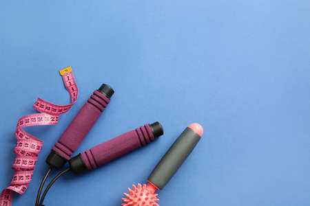 Skipping rope, measuring tape and massage roller on blue background