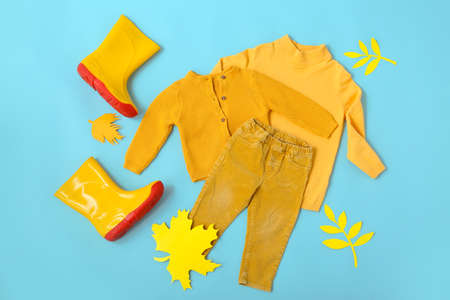 Stylish kid clothes, gumboots and autumn leaves on blue backgroundの写真素材