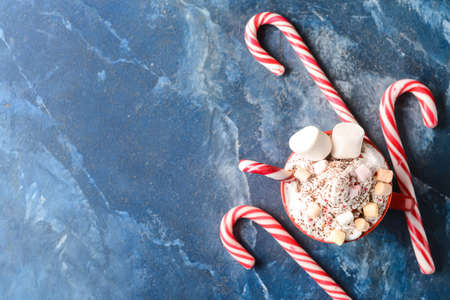 Cup of tasty cacao with marshmallows and candy canes on blue background