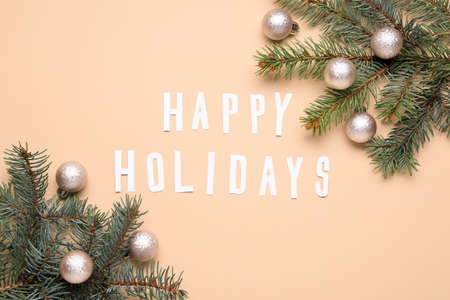 Text HAPPY HOLIDAYS, fir tree branches and Christmas balls on beige backgroundの写真素材