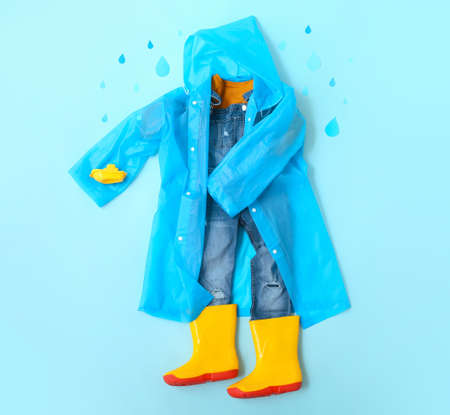Kid clothes, raincoat, gumboots and autumn decor on blue backgroundの写真素材