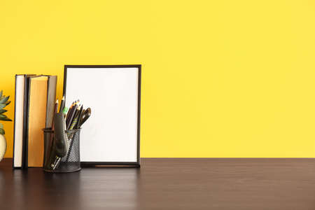 Stationery holder, books and blank photo frame near color wallの写真素材