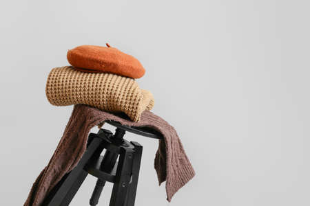 Stylish winter clothes on stool against light background