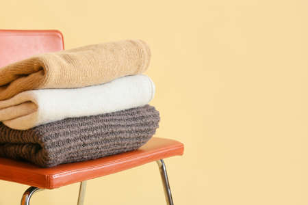 Stylish winter clothes on chair against color background