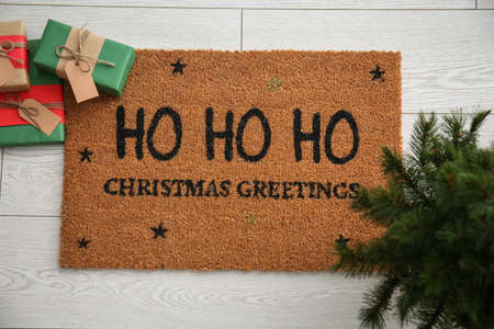 Door mat with Christmas greeting, gifts and small fir tree on white wooden floorの写真素材