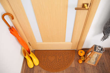 Gumboots with umbrella, pumpkins, candles and mat near wooden doorの写真素材