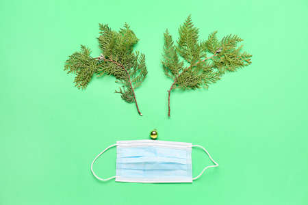 Christmas reindeer made of fir tree branches, ball and medical mask on color backgroundの写真素材