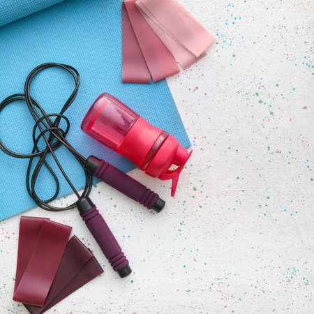 Elastic bands, skipping rope, yoga mat and bottle of water on light backgroundの写真素材