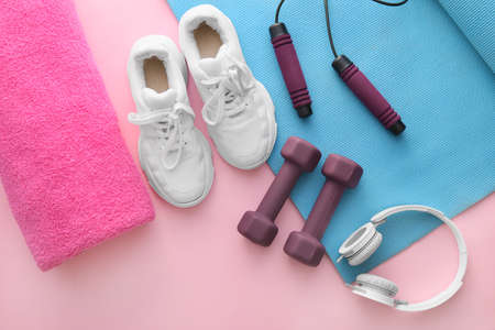 Set of sports equipment with headphones and shoes on color background